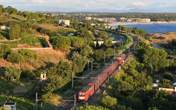 Ein Zug fährt durch eine mediterrane Landschaft.