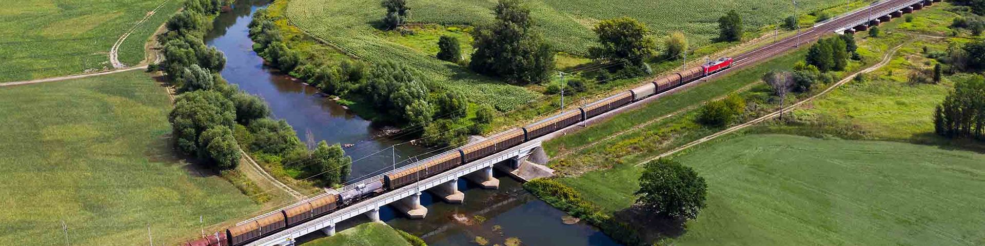 Güterzug fährt über einen Fluss inmitten grüner Landschaft.