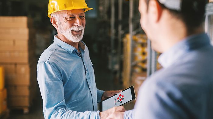 Two warehouse specialists shake hands and operate link2rail on a tablet