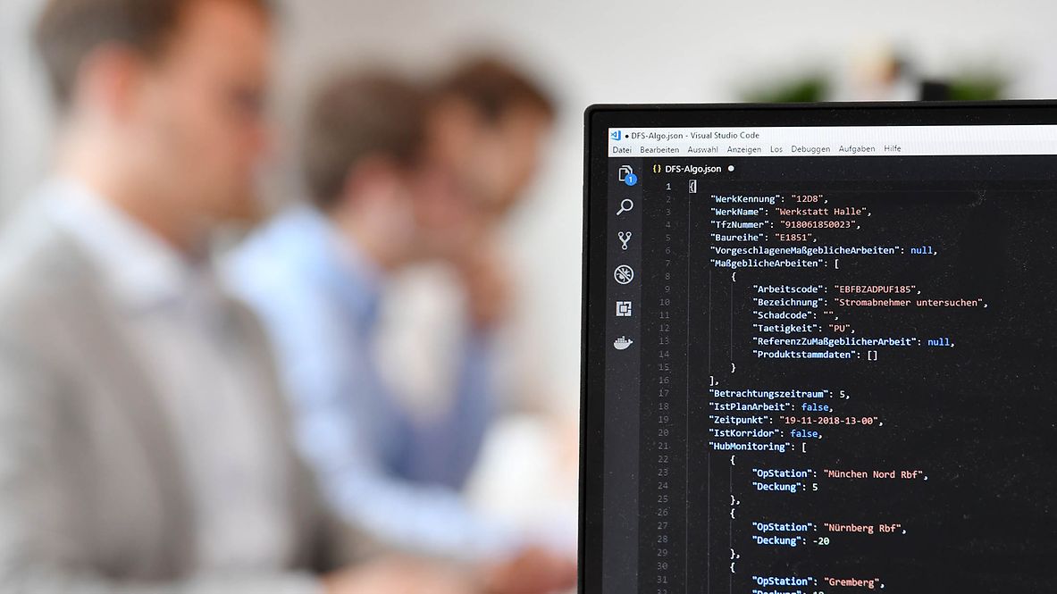 Bildschirm mit Programmierzeilen. Personen im Hintergrund