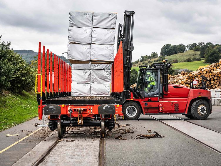 Ein modularer Güterwagen mit Rungen wird mit in Folie bepacktem Holz beladen.