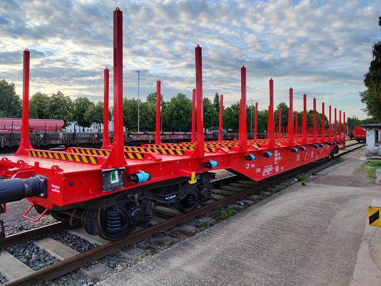 Ein leerer, roter Rungenwagen steht am Gleis.