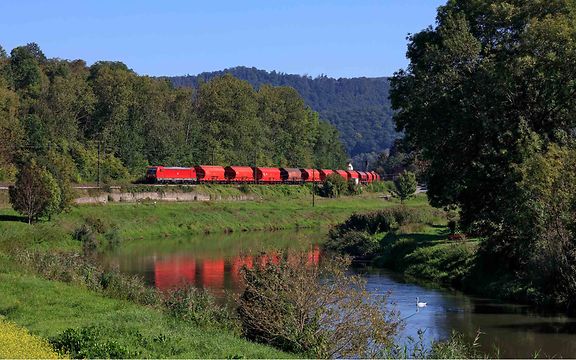 Güterzug mit Schüttgutwagen fährt durch eine grüne Landschaft.