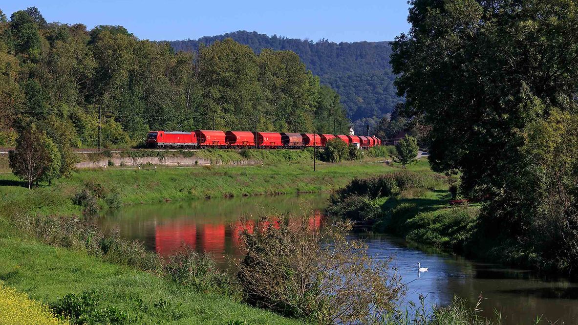 Güterzug mit Schüttgutwagen fährt durch eine grüne Landschaft.