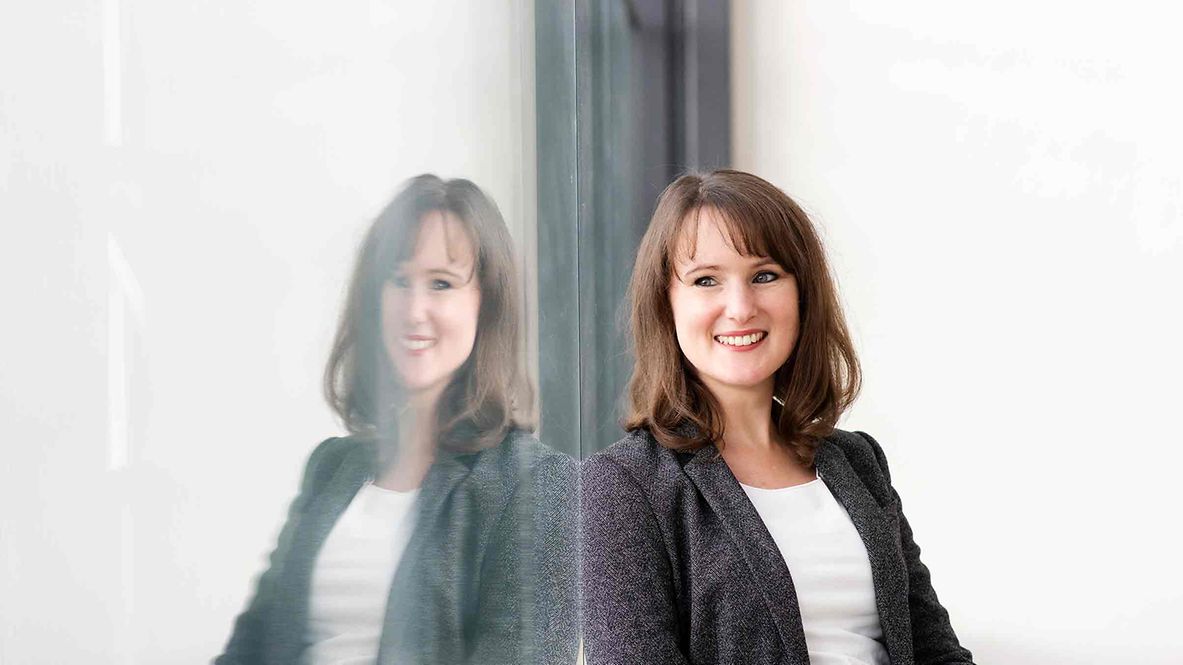 Meike Friedrich sitzt lächeln an einer spiegelnden Scheibe, in der man sie ebenfalls sieht.