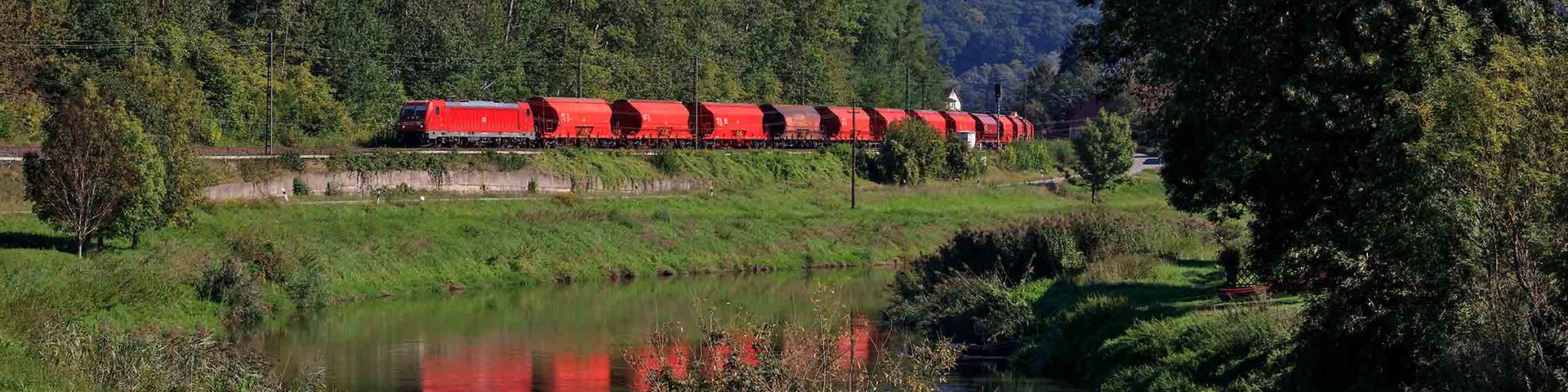 Güterzug mit Schüttgutwagen fährt durch eine grüne Landschaft.