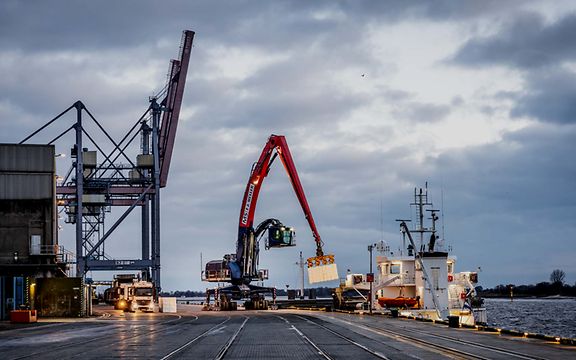 Ein Kran im Hafen lädt Güter auf ein Schiff.