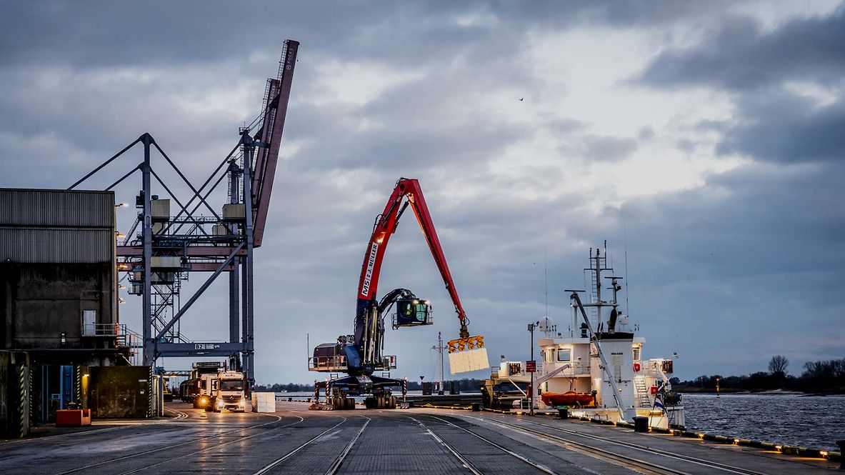 Ein Kran im Hafen lädt Güter auf ein Schiff.