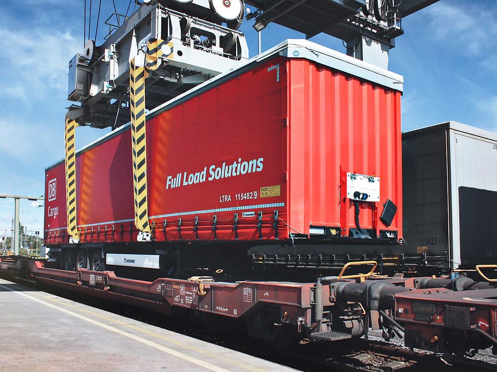 Ein kranbarer Trailer von DB Cargo FLS wird auf einem Güterwagen platziert.