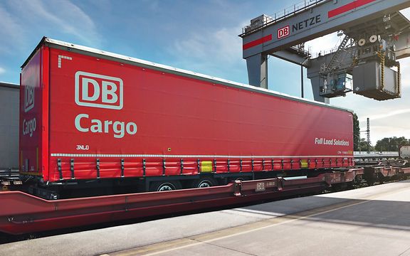 Ein kranbarer Trailer von DB Cargo FLS wird von einem Kran verladen.