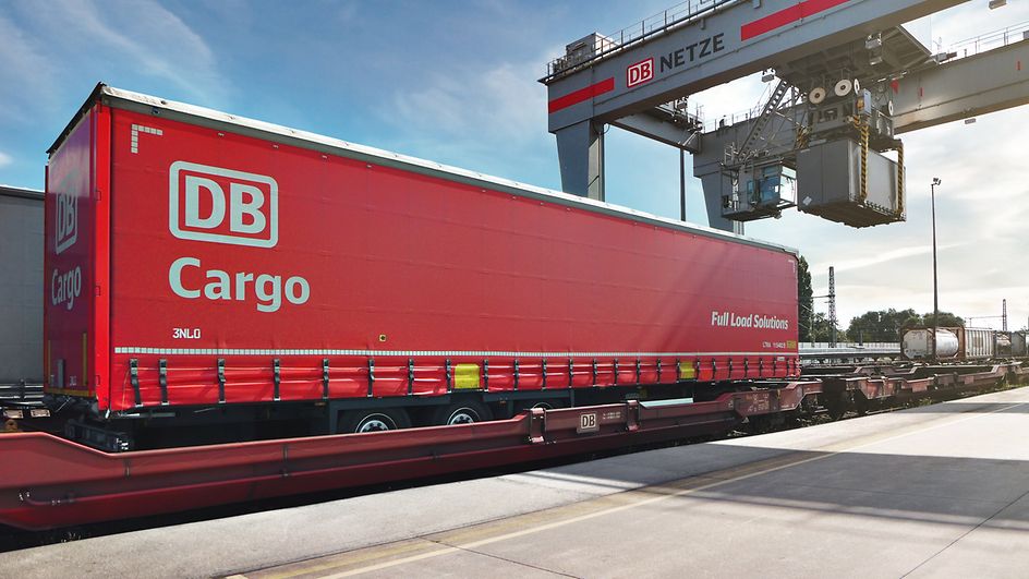 Ein kranbarer Trailer von DB Cargo FLS wird von einem Kran verladen.