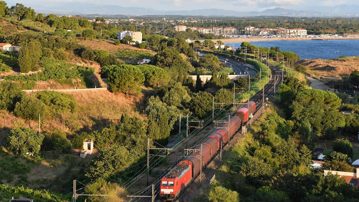 Ein Zug fährt durch eine mediterrane Landschaft.