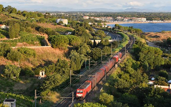 A train travels through a Mediterranean landscape.