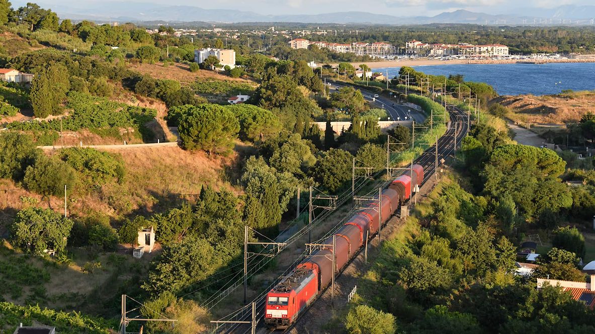 A train travels through a Mediterranean landscape.