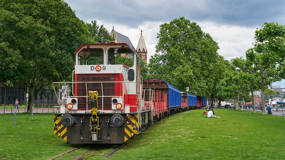 Eine Lok zieht Güterwagen am Frankfurter Mainufer.