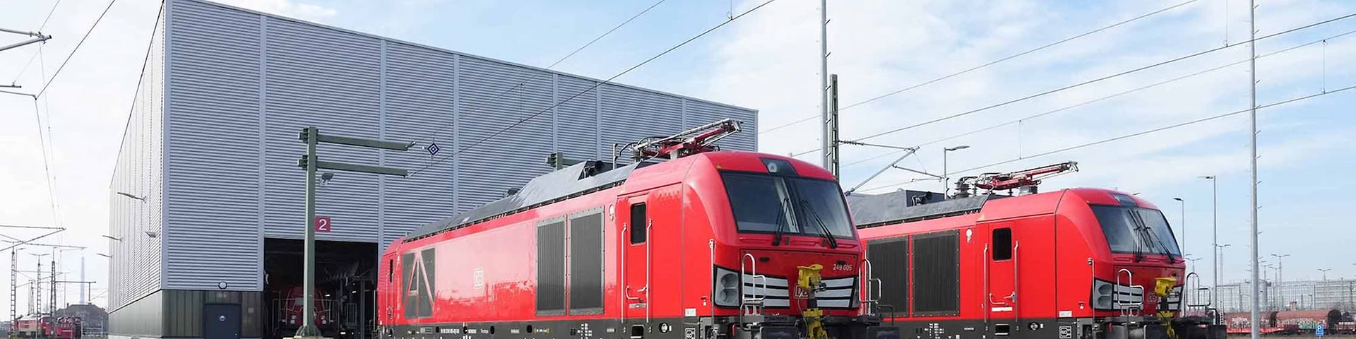 Zwei Zweikraftloks stehen nebeneinander vor einer Halle.