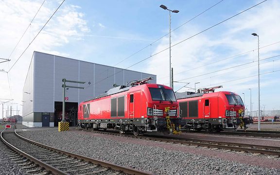 Two dual-mode locomotives next to each other in front of a maintenance shed.