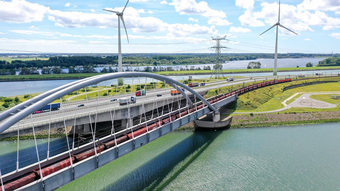 Eisenbahnbrücke mit Windrädern im Hintergrund.