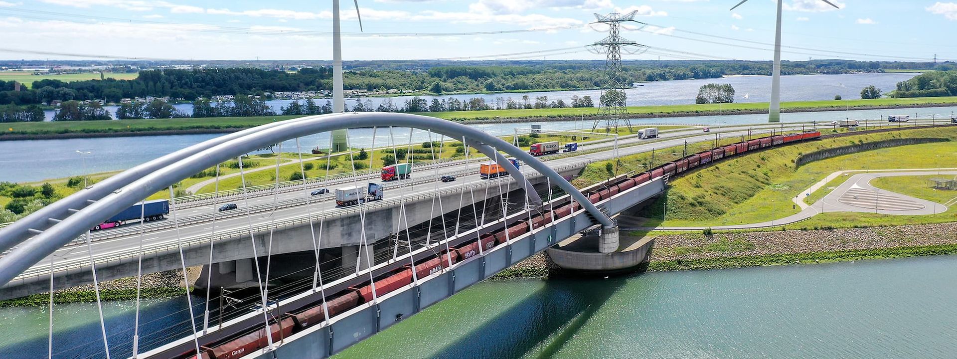 Eisenbahnbrücke mit Windrädern im Hintergrund.