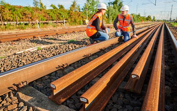 Zwei DB-Mitarbeitende hocken an den Gleisen, neue Gleise liegen vor ihnen.