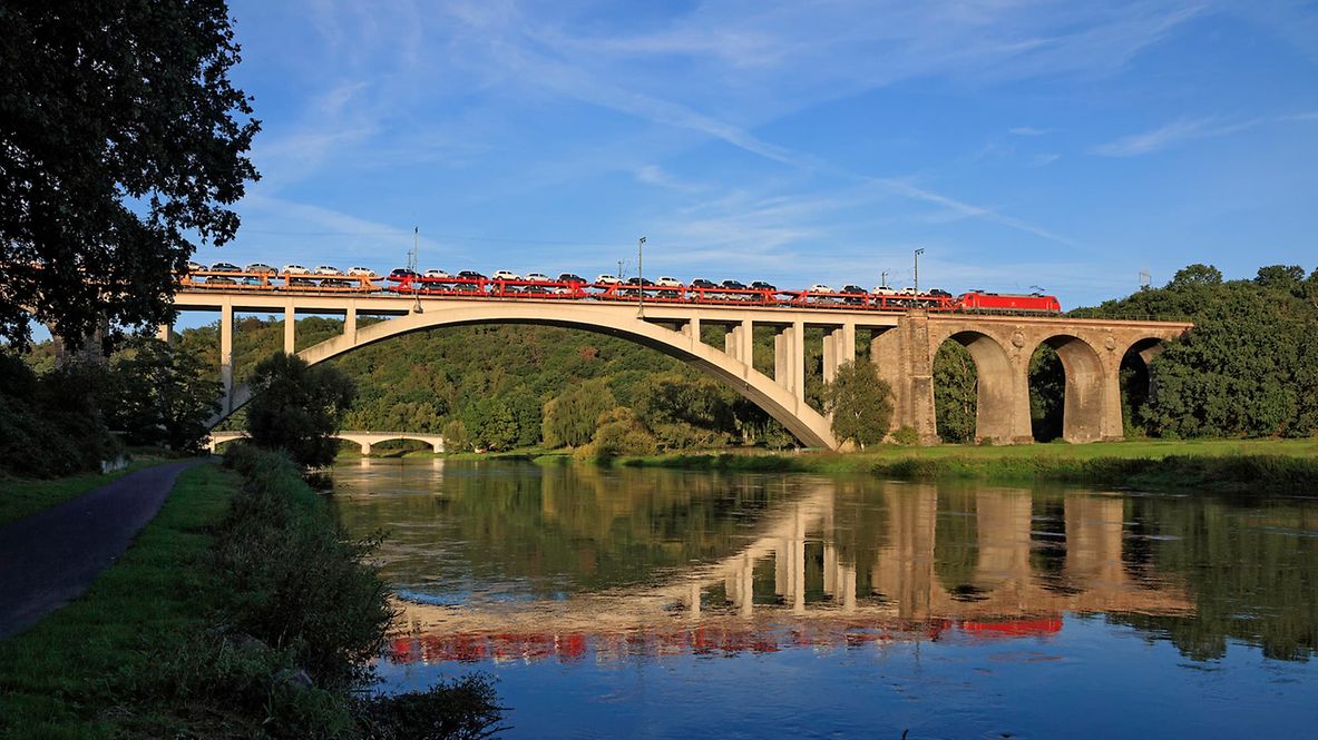 A freight train with several freight cars crosses a bridge under a blue sky.