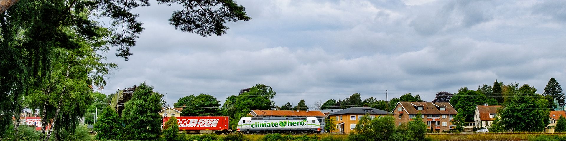 Lakescape with traditional Scandinavian houses, a freight train with the label 'climate hero' in the background