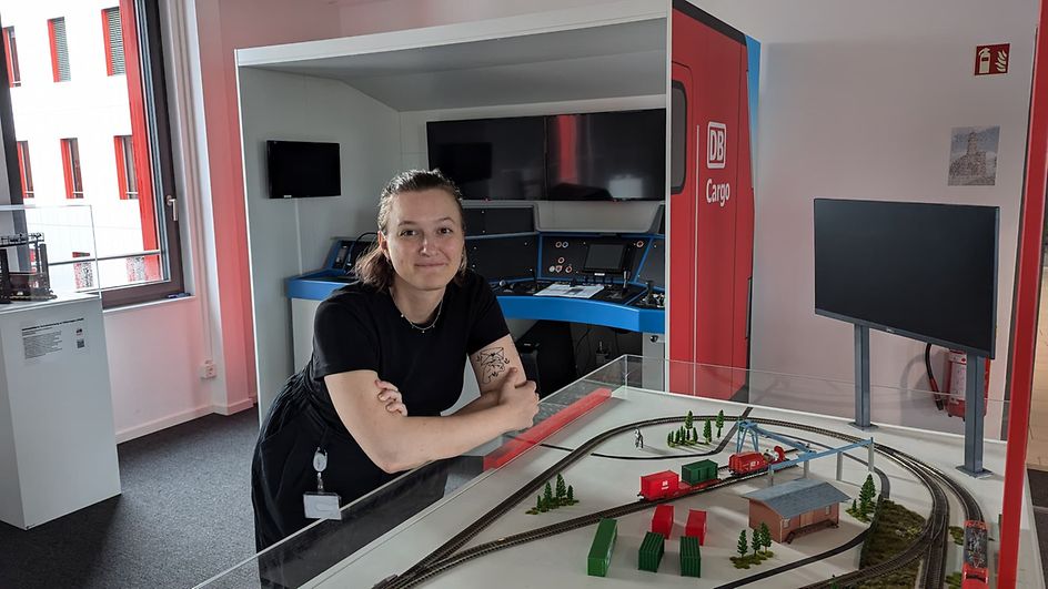 A woman in dark clothing leans on a glass display case with a miniature train.