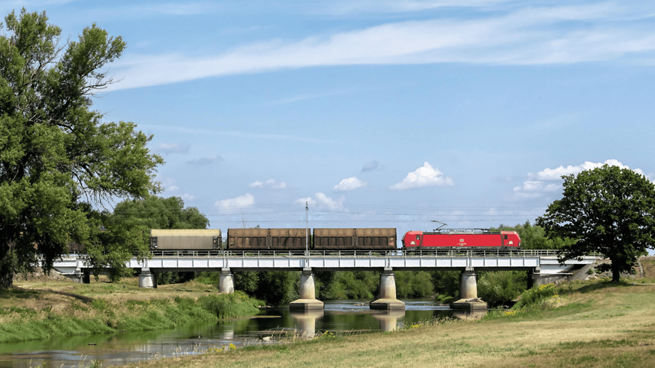 DB Cargo's red locomotive pulls a train with sliding-wall wagons over a bridge