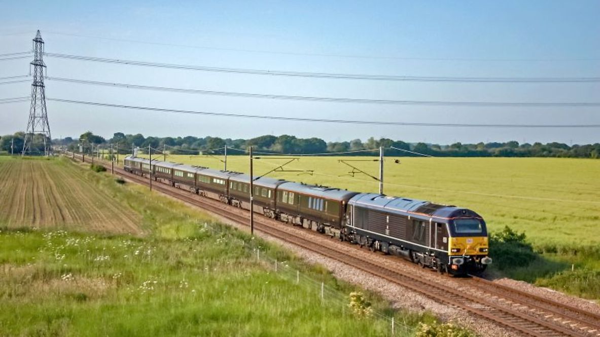 Royal train drives through a green landscape.
