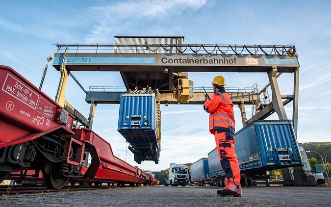 Personal steht auf Containerbahnhof und leitet die Verladung von Sattelaufliegern auf einen Flachwagen
