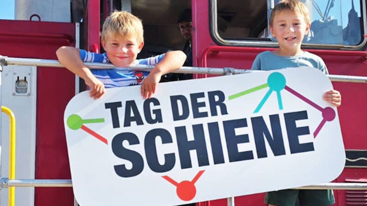 Kinder stehen auf einer Lok und halten zusammen ein Tag der Schiene Poster in den Händen