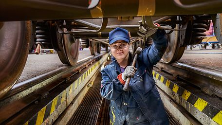 Frau im blauen Overall unterm Zug mit Hammer in der Hand