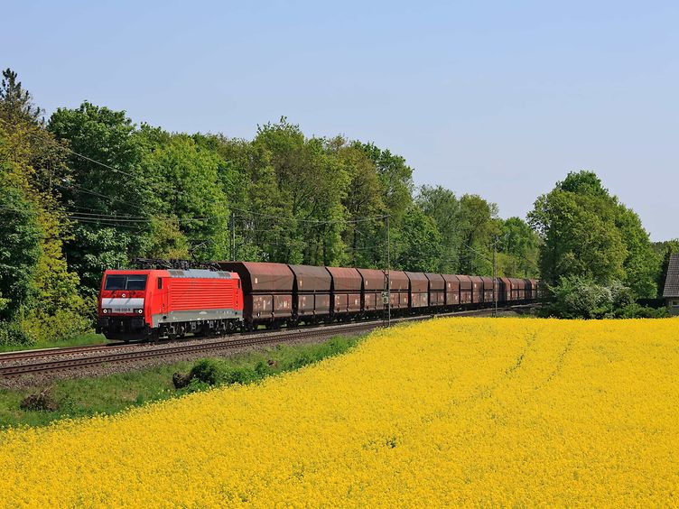 Ein Güterzug mit offenen Schüttgutwagen fährt an einem Rapsfeld vorbei