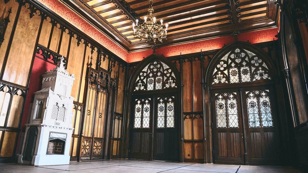 Großer Raum mit edlen Holzvertäfelungen, verzierten Fenstern und Kronleuchtern