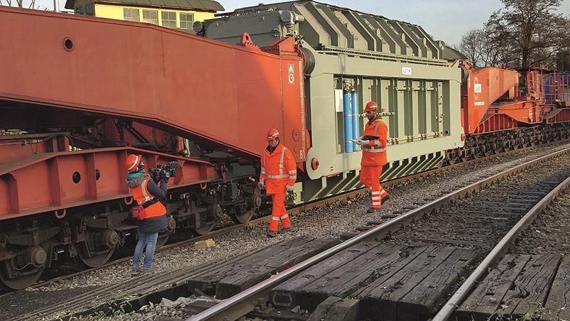 Drei Bahnarbeiter neben einem Schwertransport