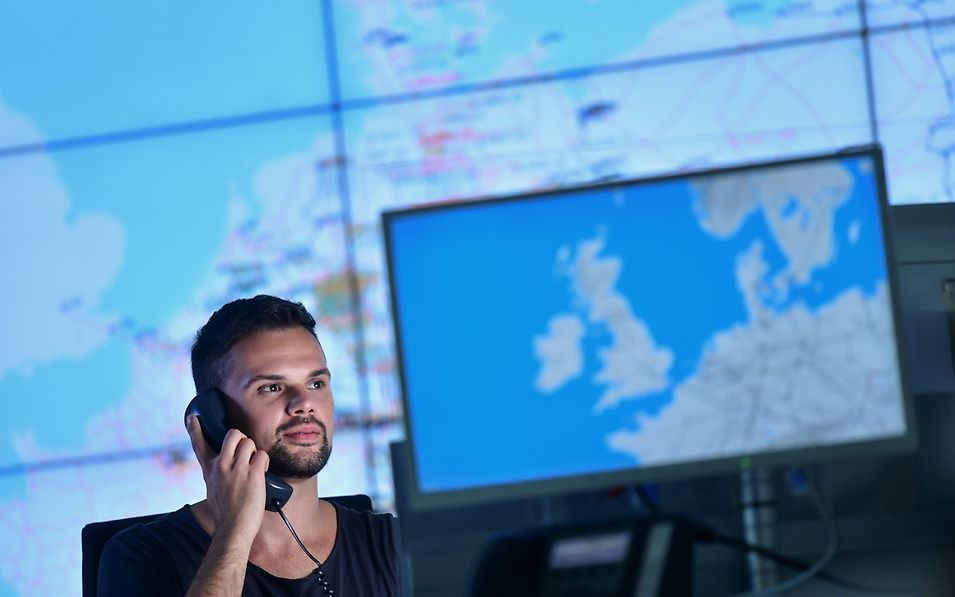 Mann im Büro am Telefon vor großen Europakarten