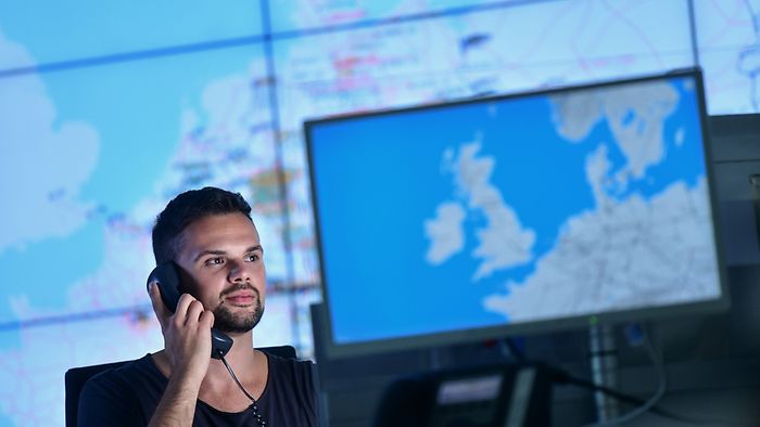 Mann im Büro am Telefon vor großen Europakarten