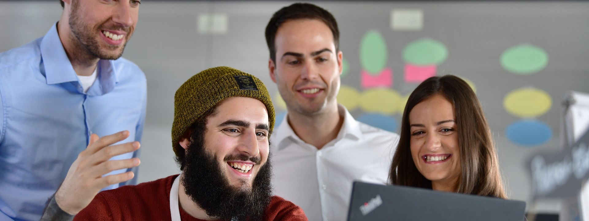 Four employees watch at one screen at the office.