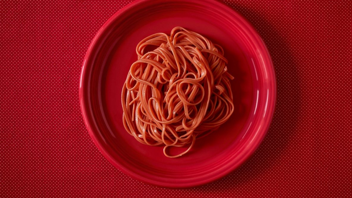 Roter Teller mit Pasta in Tomatensoße auf rotem Tischtuch