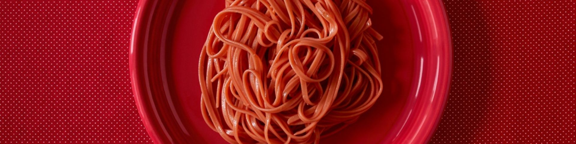 Roter Teller mit Pasta in Tomatensoße auf rotem Tischtuch