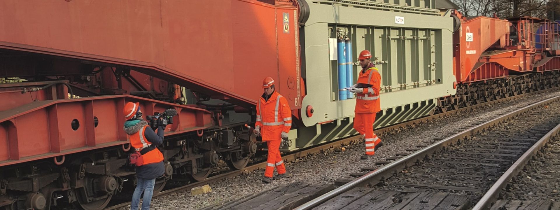 Drei Bahnarbeiter neben einem Schwertransport